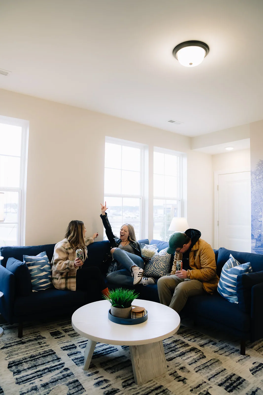 Three guests on a navy sectional in a bright living room, one with an arm raised
