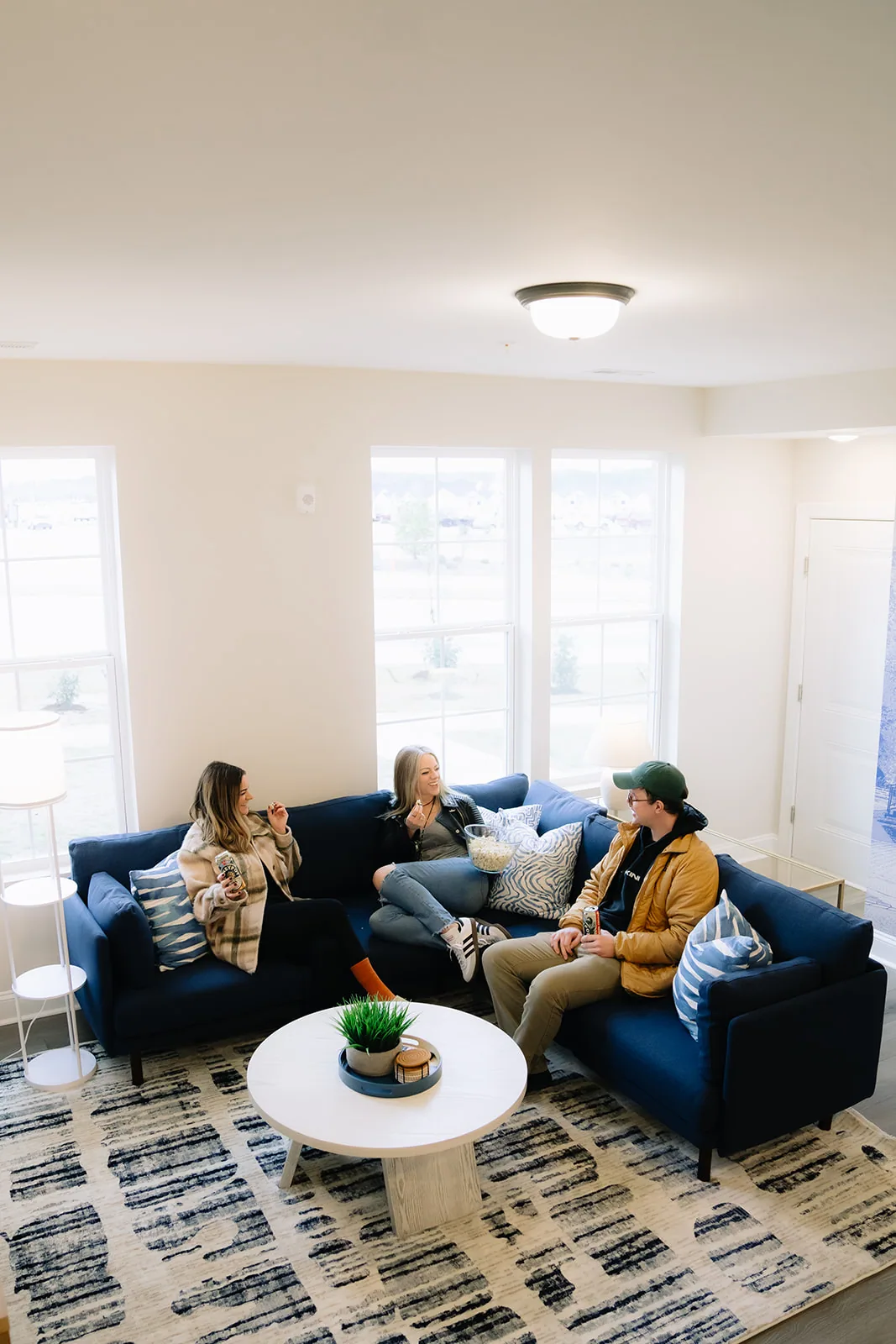 Living room with three guests seen from the kitchen side, windows along two walls