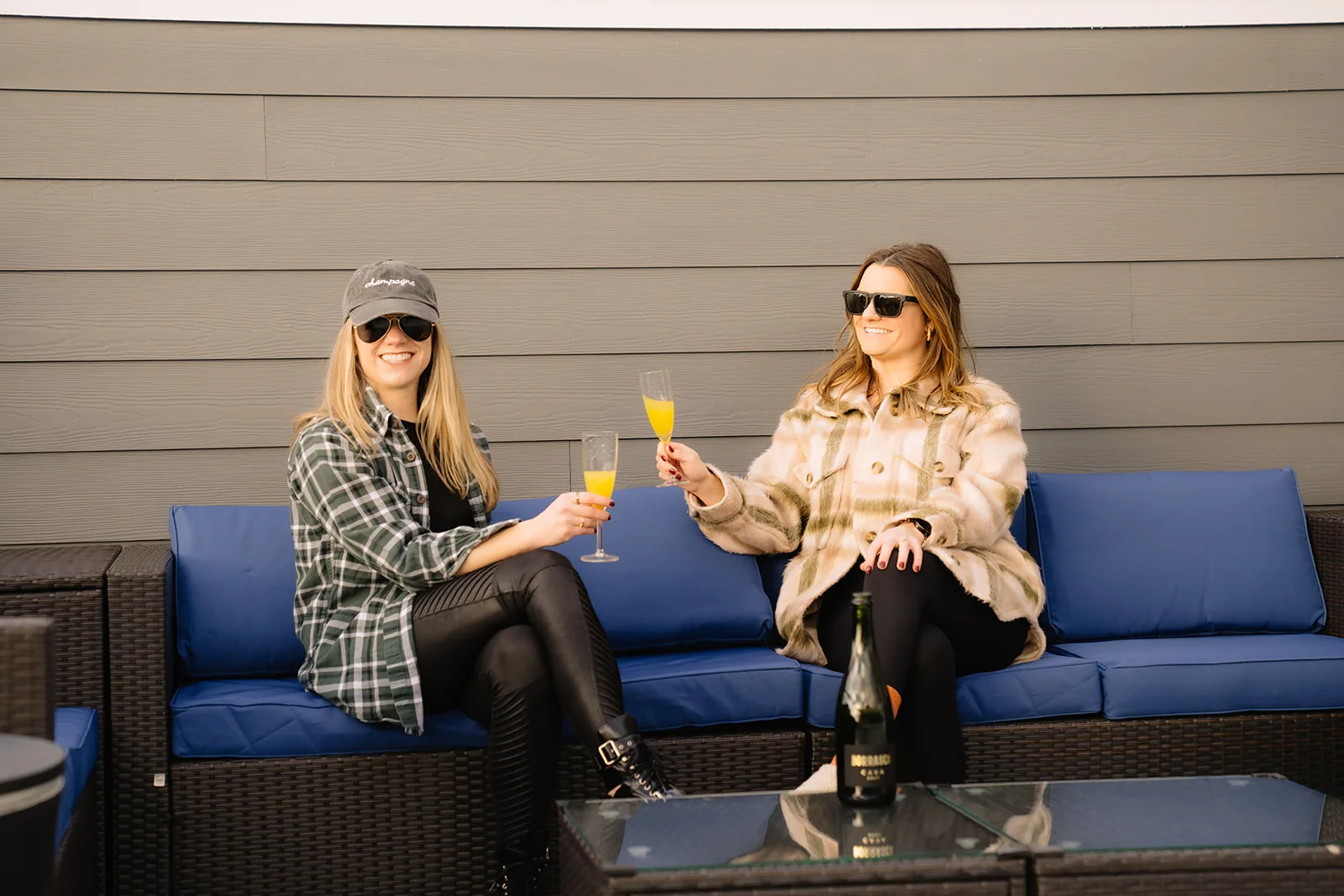 Two women toasting with mimosas on a navy rooftop sectional