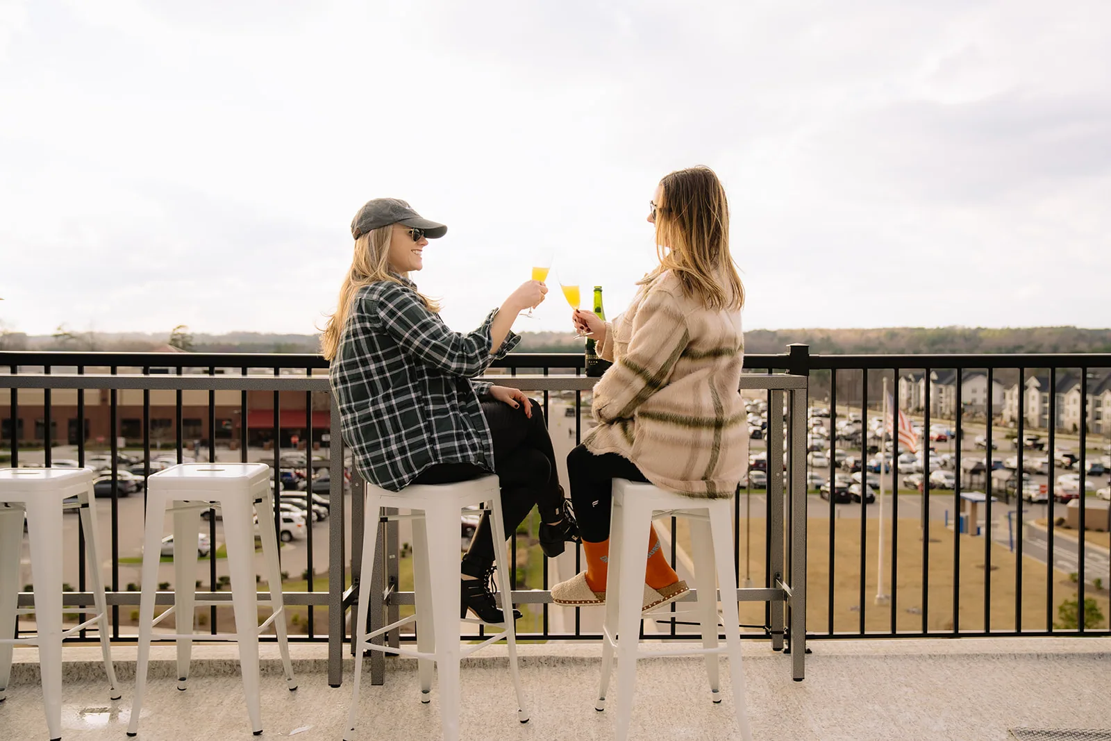 Two guests on white bar stools at the rooftop railing with the retail center below