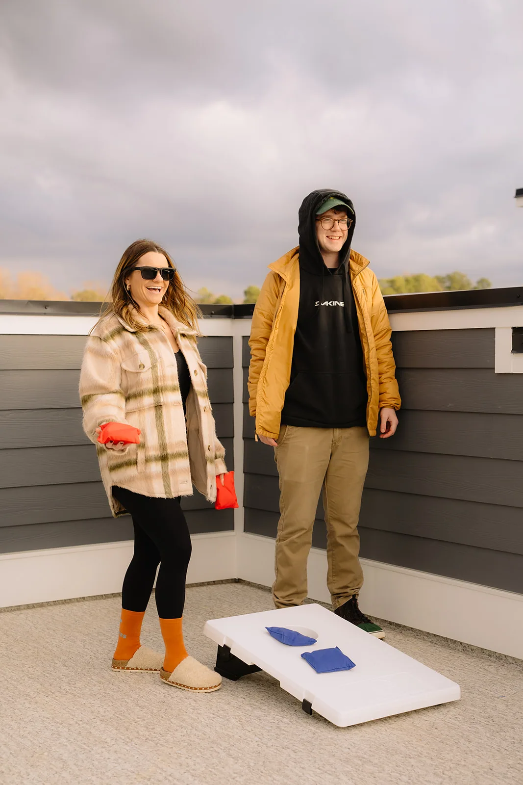Man and woman standing beside a cornhole board on a rooftop deck