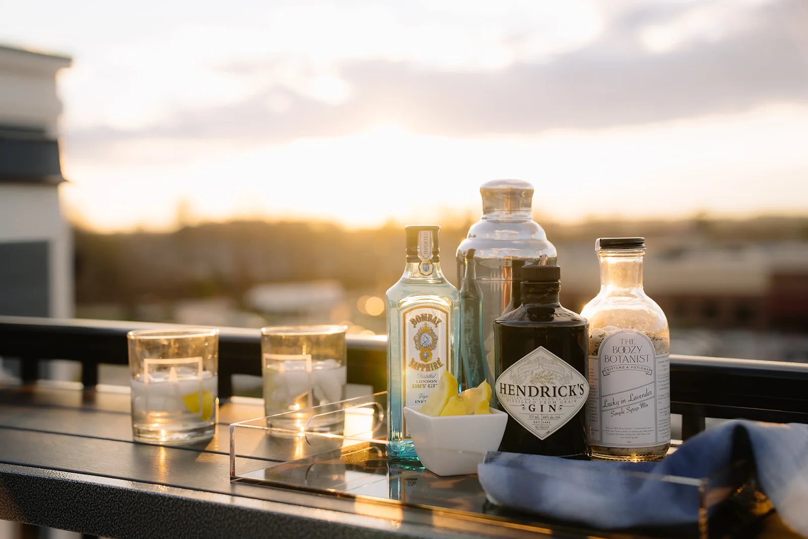 Gin bottles and cocktail glasses lined along a rooftop ledge at sunset