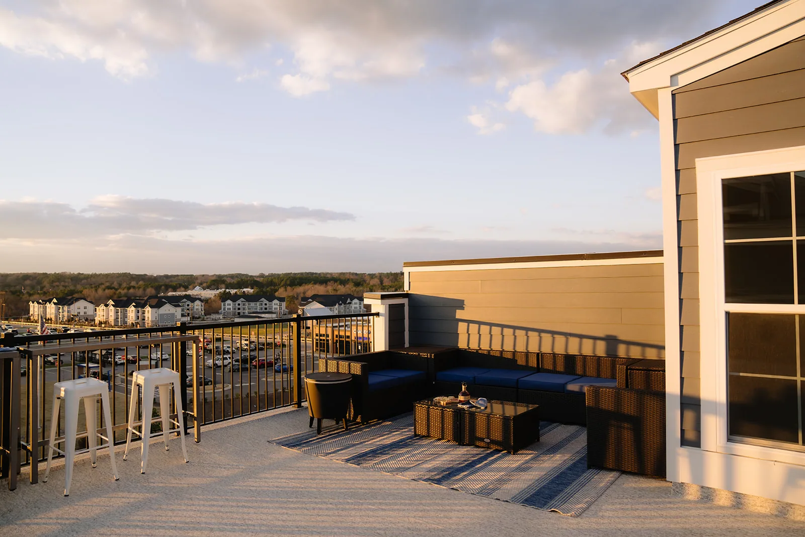 Empty rooftop deck with blue seating, bar stools and a striped rug in evening light