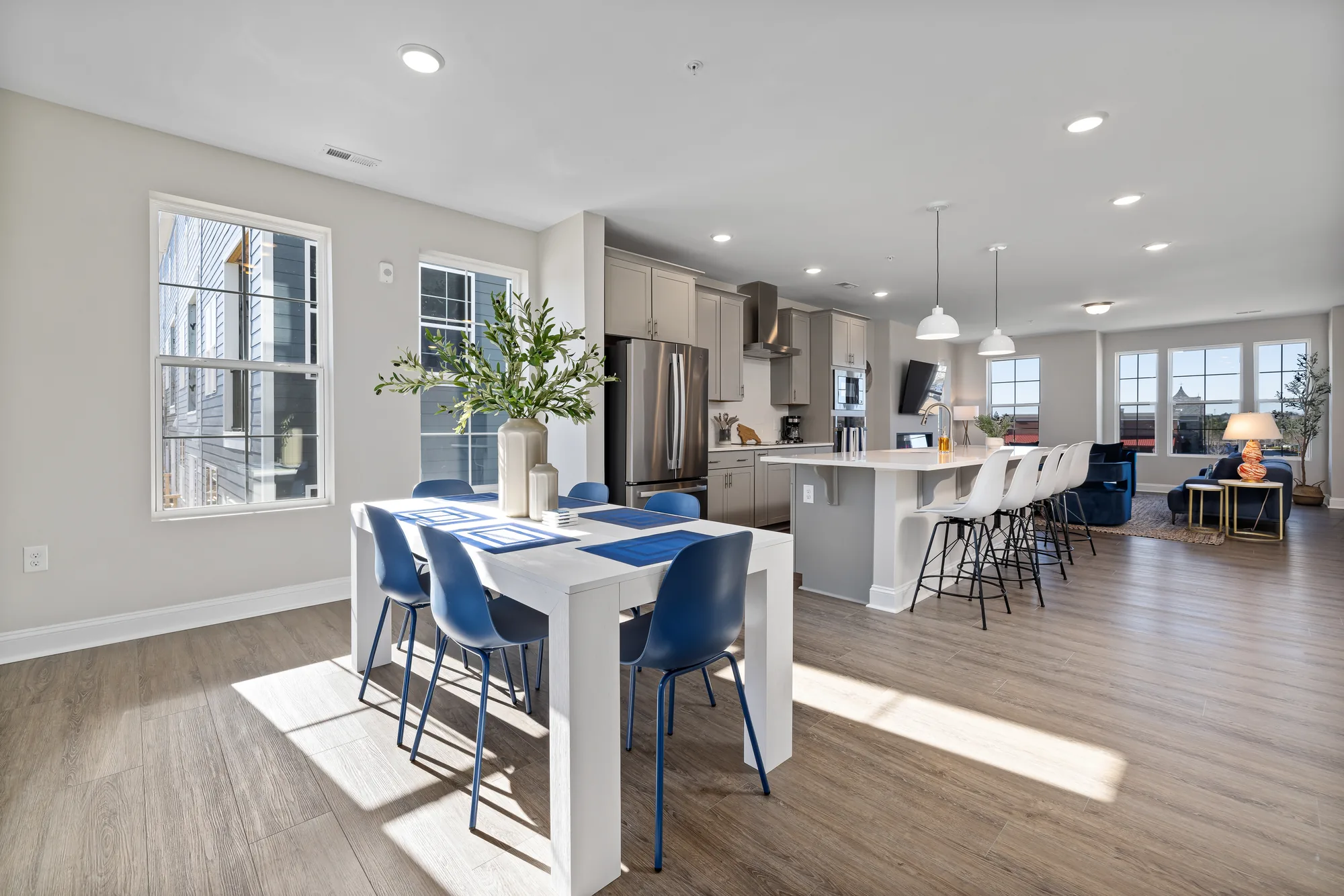Dining table with blue chairs looking toward the kitchen island and living area, tighter crop