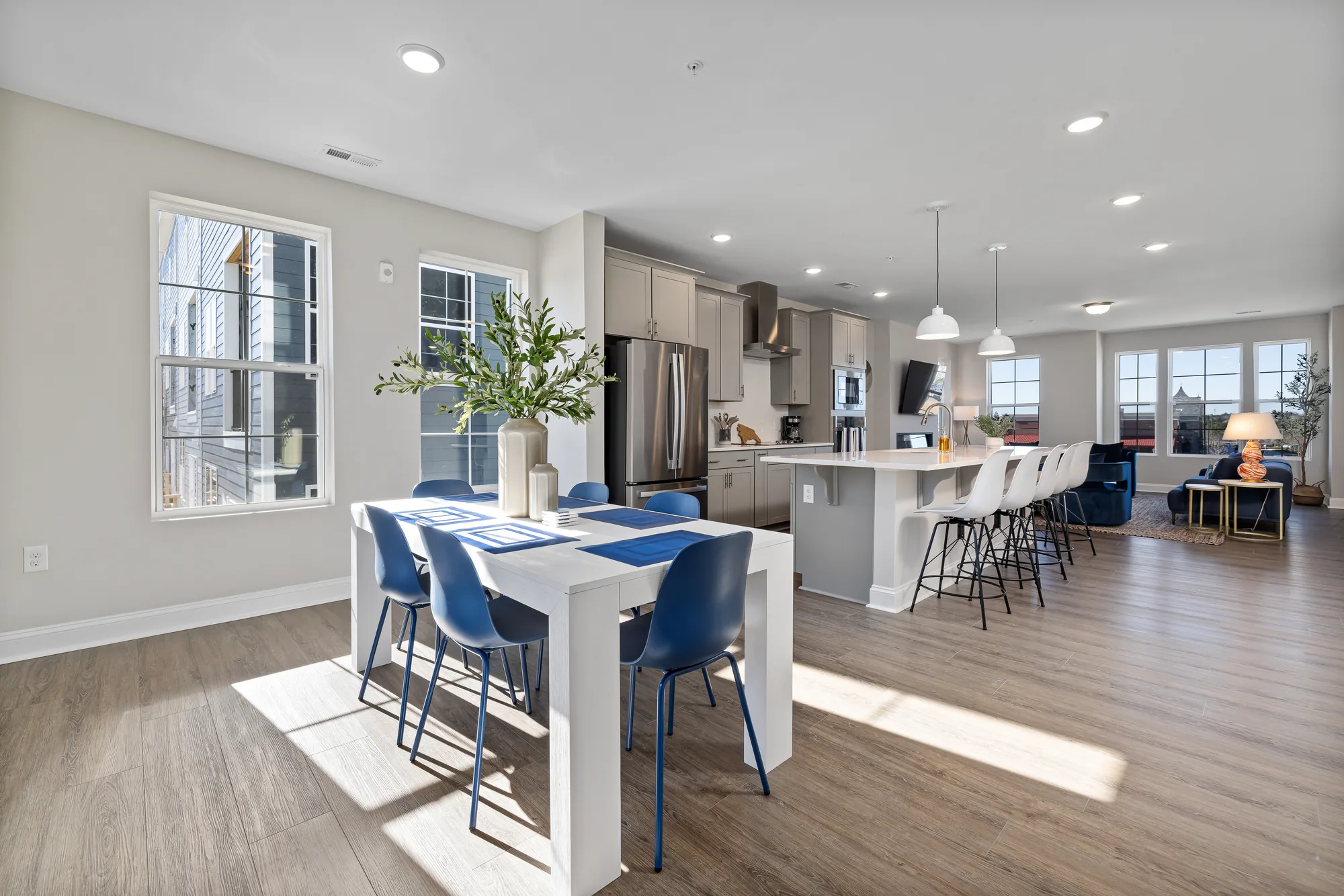 Dining table in the foreground with the kitchen island and blue living room seating beyond