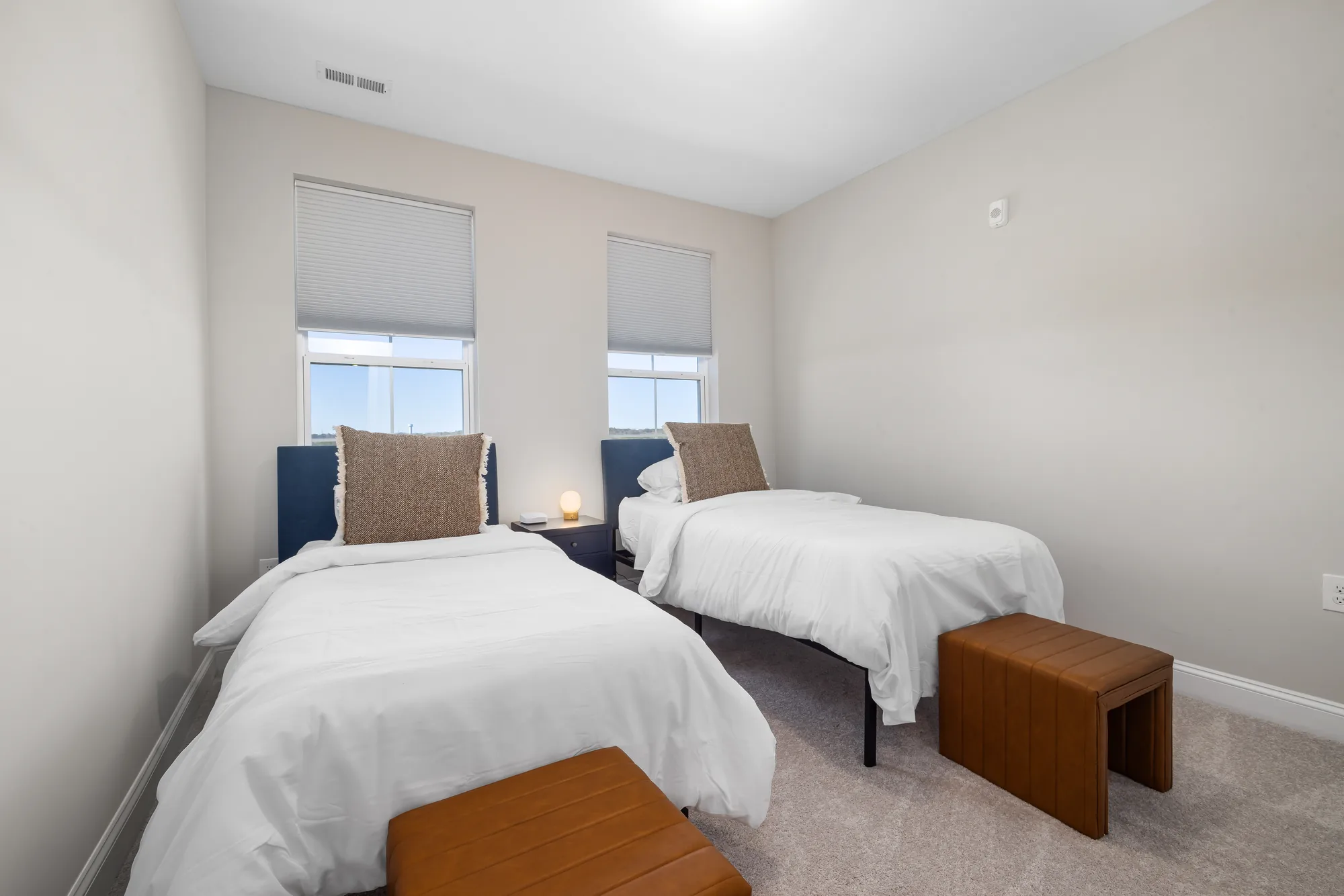 Two twin beds with navy headboards, white bedding and tan pillows either side of a bench