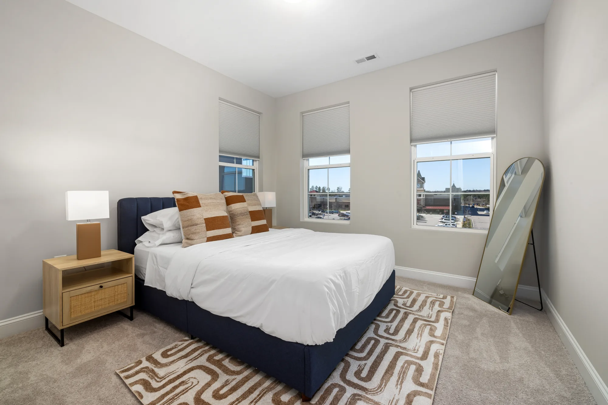 Navy bed with white bedding and tan pillows, wood nightstands and a leaning floor mirror