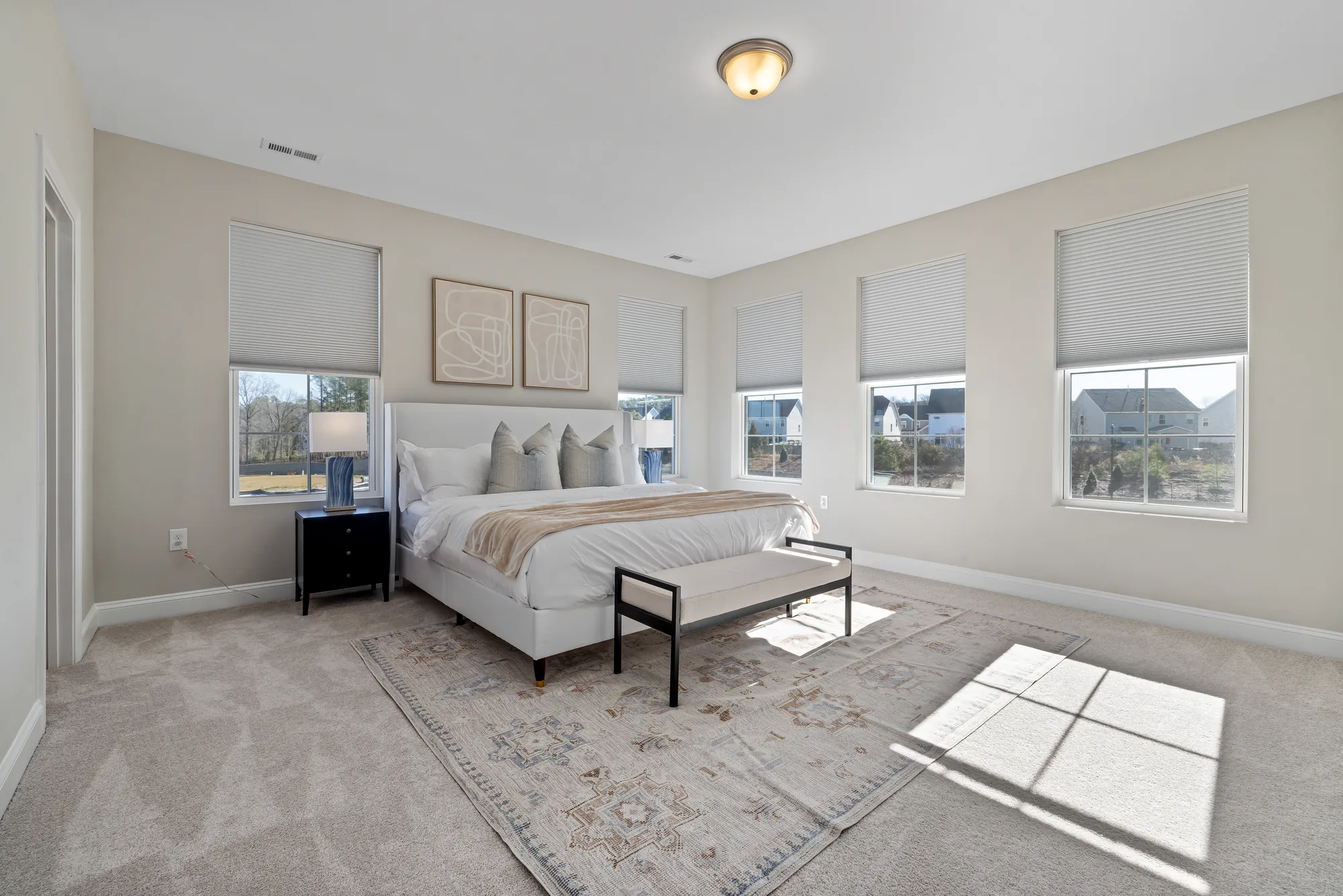 Primary bedroom with a cream upholstered bed, bench and patterned rug under three windows