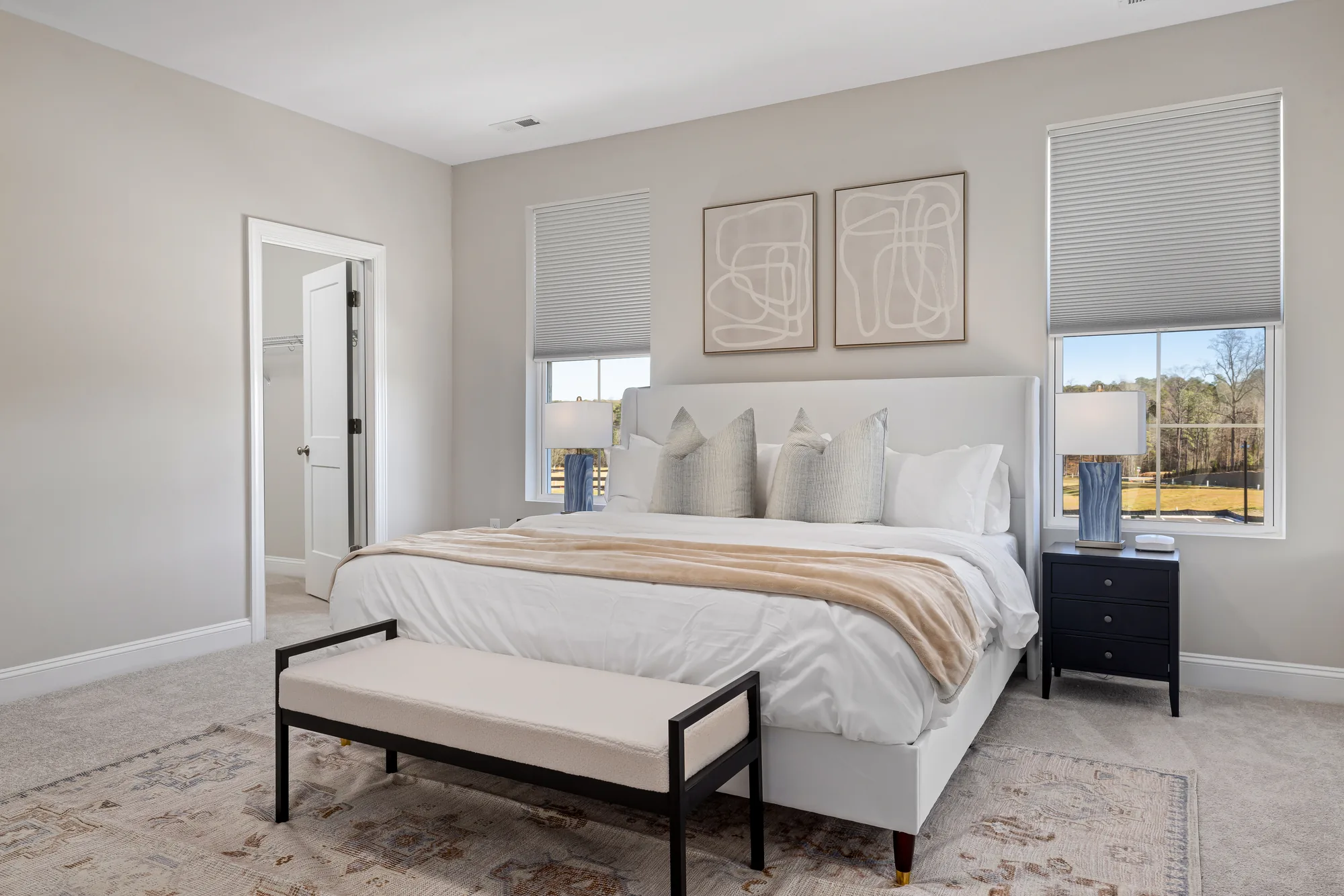 White upholstered bed under a pair of framed prints with a bench and a black nightstand