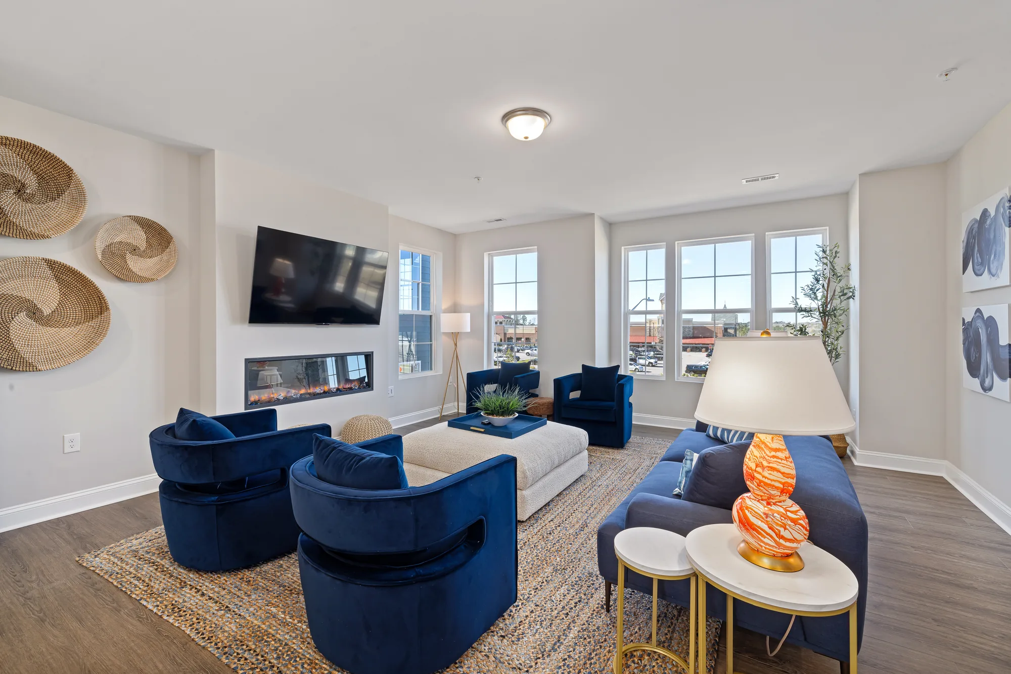 Wide living room with blue sofa and swivel chairs, woven wall discs and windows on two walls