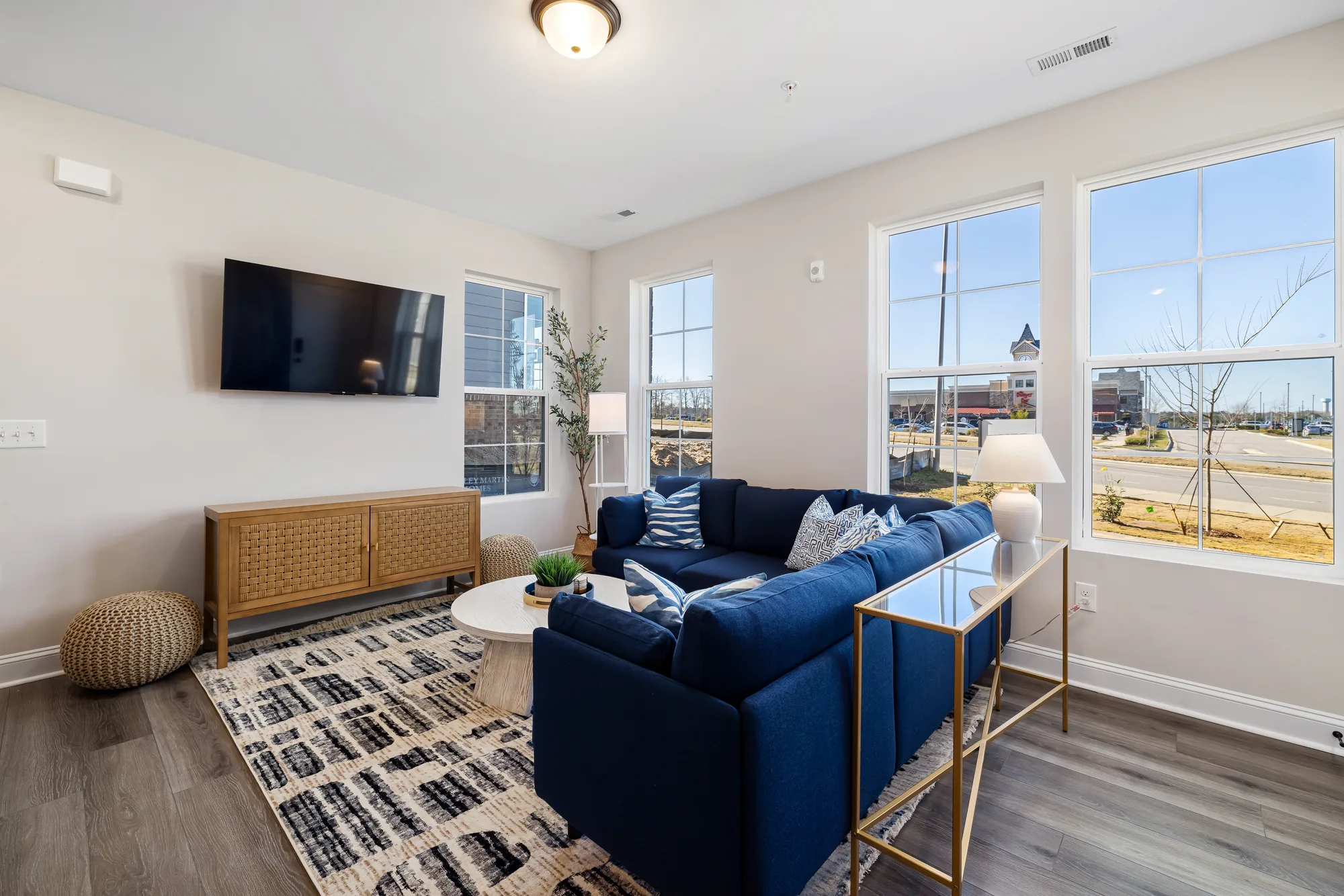 Blue sectional facing a wall mounted television with a woven console and a patterned rug