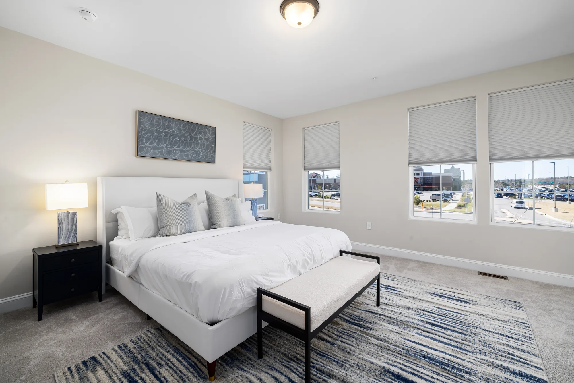 White upholstered bed with a navy canvas above it, a bench at the foot and a striped rug