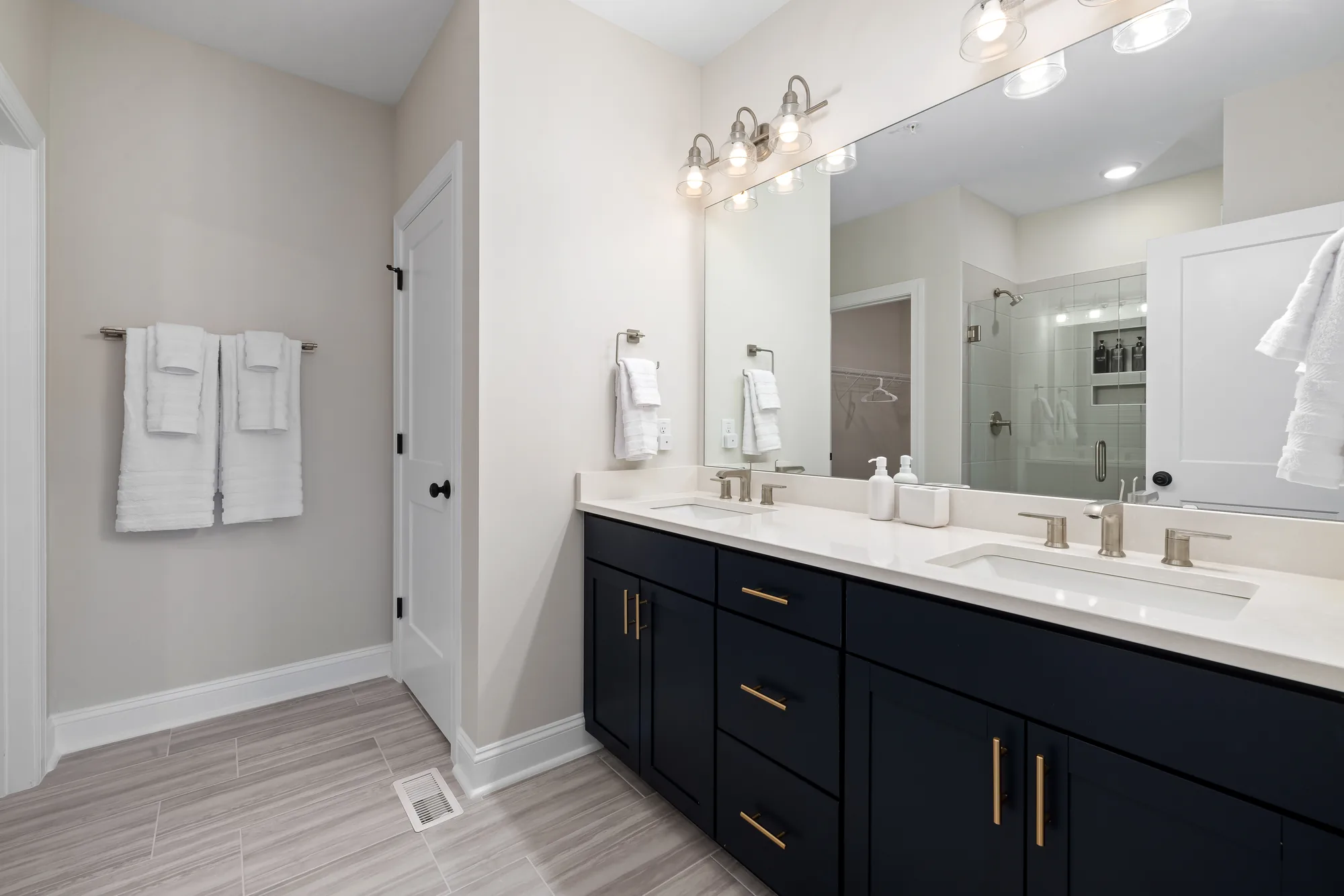Navy double vanity with a wide mirror and a light bar, towels on the rail, shower beyond