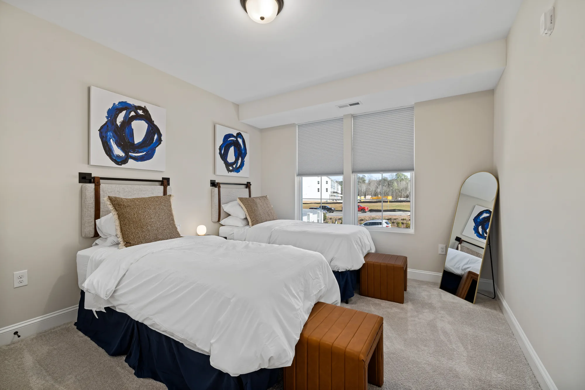 Two twin beds with a pair of navy abstract canvases above and a leather bench between