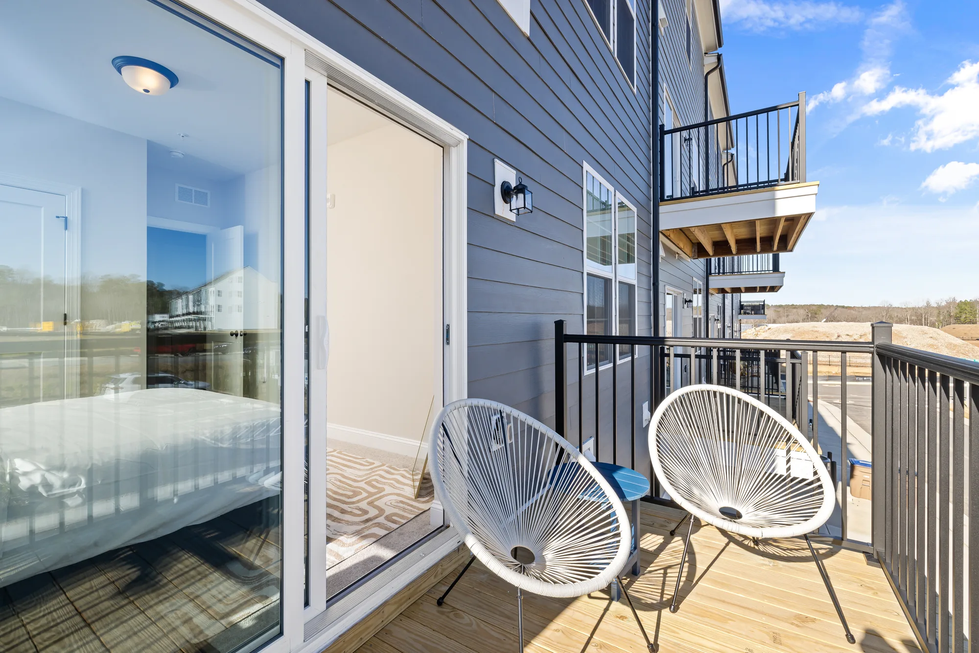 Balcony through a sliding door with two white woven Acapulco chairs against blue siding